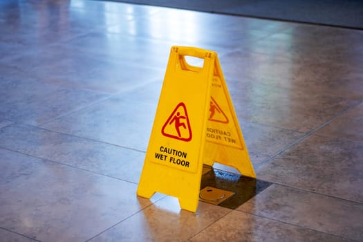 There is a yellow caution wet floor sign placed on a tiled floor surface, warning about the potential hazard. The sign stands out with its vibrant color against the tiles