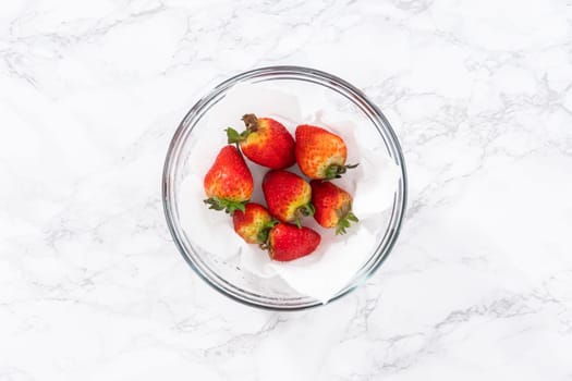 Freshly washed and dried strawberries are carefully arranged in a glass bowl lined with paper towel, ready for snacking or further use.