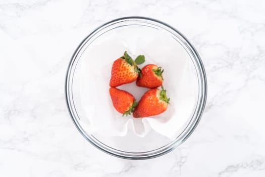 Freshly washed and dried strawberries are carefully arranged in a glass bowl lined with paper towel, ready for snacking or further use.