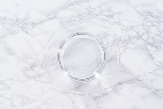 A spacious glass mixing bowl filled with water sits prepared to gently cleanse a batch of ripe strawberries, ensuring they are pristine before drying or storage.