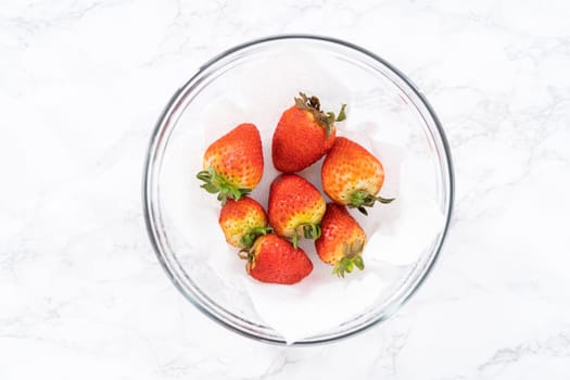 Freshly washed and dried strawberries are carefully arranged in a glass bowl lined with paper towel, ready for snacking or further use.