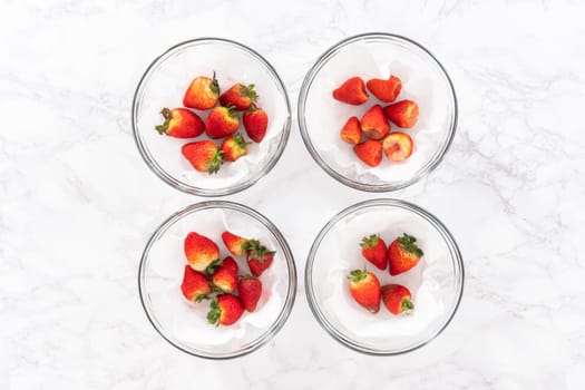 Bright red strawberries, interspersed with signs of mold, rest in a glass bowl lined with a paper towel on a white napkin, indicating improper storage techniques.