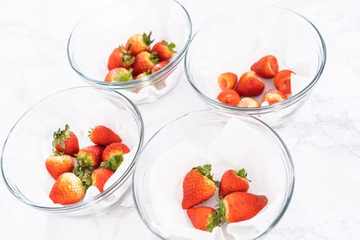 Freshly washed and dried strawberries are carefully arranged in a glass bowl lined with paper towel, ready for snacking or further use.