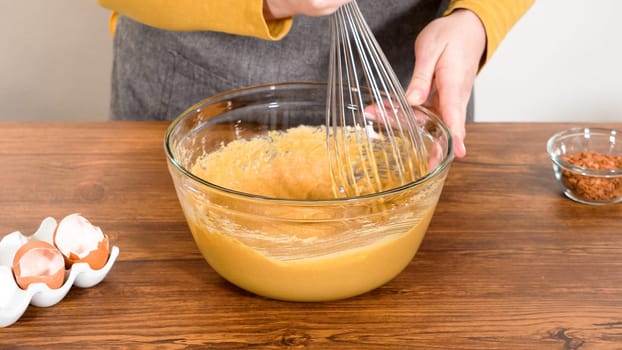 In a glass mixing bowl, a large hand whisk expertly blends the ingredients for a delectable gingerbread bundt cake with caramel frosting.