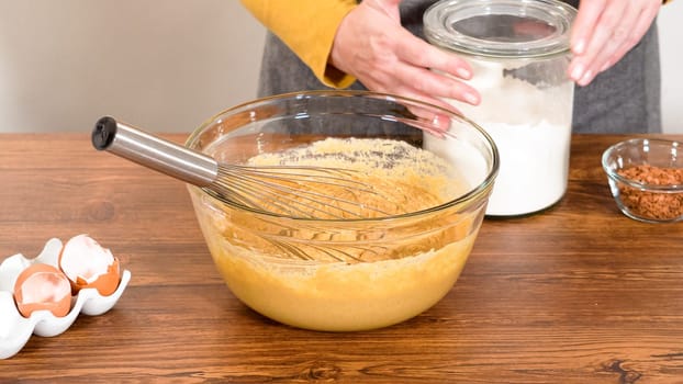 In a glass mixing bowl, a large hand whisk expertly blends the ingredients for a delectable gingerbread bundt cake with caramel frosting.