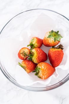 Freshly washed and dried strawberries are carefully arranged in a glass bowl lined with paper towel, ready for snacking or further use.