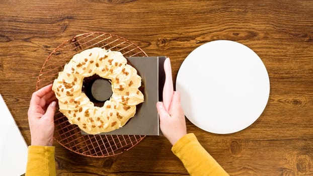 Flat lay. Carefully placing the gingerbread bundt cake, adorned with salted caramel frosting and gingerbread sprinkles, into a white paper bundt cake box with a clear window for gifting.