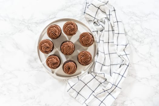 Flat lay. Freshly baked cupcakes have been masterfully infused with rich caramel and adorned with velvety chocolate frosting, all elegantly presented on a pristine white serving plate.