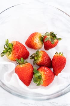 Freshly washed and dried strawberries are carefully arranged in a glass bowl lined with paper towel, ready for snacking or further use.