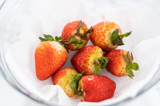 Freshly washed and dried strawberries are carefully arranged in a glass bowl lined with paper towel, ready for snacking or further use.