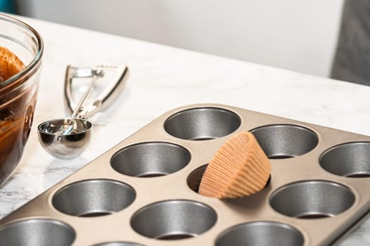 Getting ready to bake delicious chocolate cupcakes, we carefully line the cupcake pan with paper liners, ensuring a delightful treat awaits.