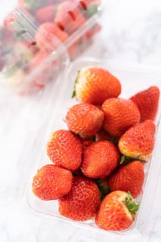 Fresh strawberries are showcased in their original store-bought plastic container, resting on a kitchen counter, ready to be washed, eaten, or stored.