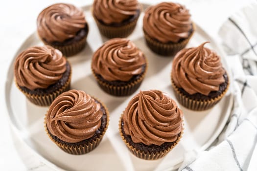 Freshly baked cupcakes have been masterfully infused with rich caramel and adorned with velvety chocolate frosting, all elegantly presented on a pristine white serving plate.