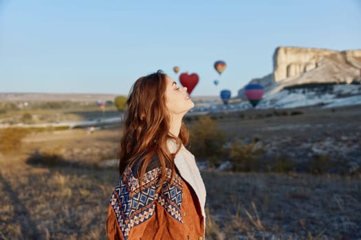 Woman admiring hot air balloons flying over vibrant field on a sunny day