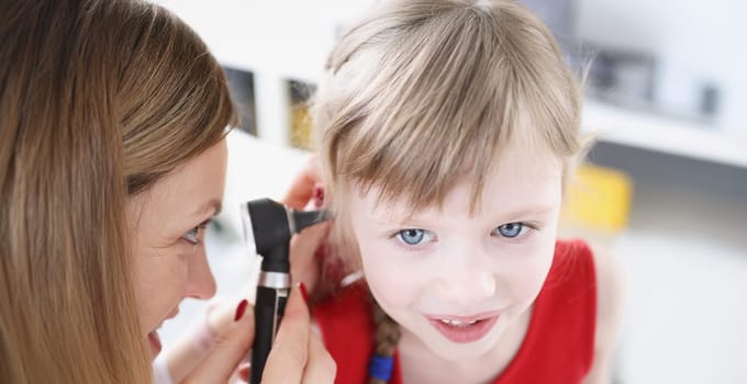 Female doctor conducts examination of ear of little girl. Baby medical services concept