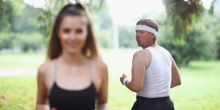 Fat man in sportswear looking at young girl jogging in park. Outdoor sports training concept