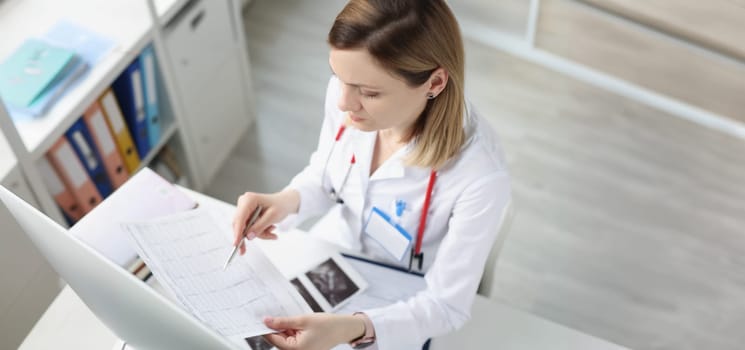 Doctor sitting at table and looking at cardiogram in clinic. Diagnostics and treatment of angina pectoris myocardial infarction concept