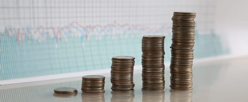 Stacks of coins increasing in row against background of financial indicators. Most profitable and most unprofitable investment projects concept