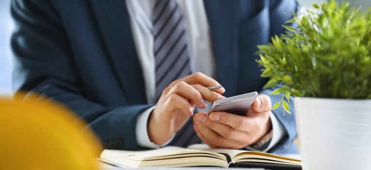 Businessman holds smartphone in his hands and diary is on table. Drawing up and planning business tasks concept
