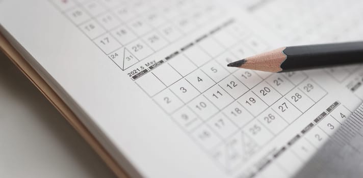 Sharp black pencil lying on calendar closeup. Scheduling action concept