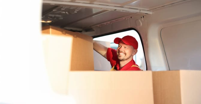 Male courier putting cardboard boxes in car. Fast delivery of household appliances concept