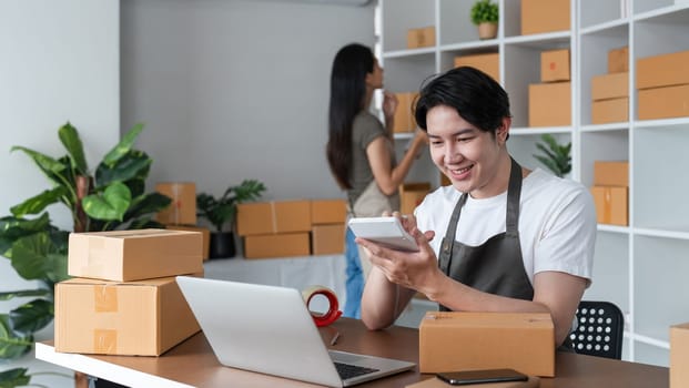 A young couple working together to pack boxes and manage their online sales business from a modern home office.