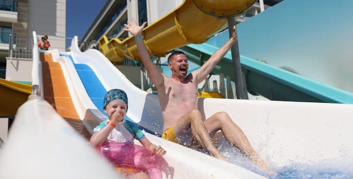 Joyful dad and daughter go down slide in water park. Summer vacation and vacation with children concept