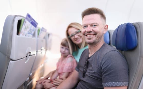 Smiling parents with child are sitting in aircraft cabin. Moving with family to another country concept