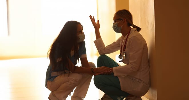 Two frustrated doctors in protective masks sit in hallway. Burnout syndrome in work of doctors concept