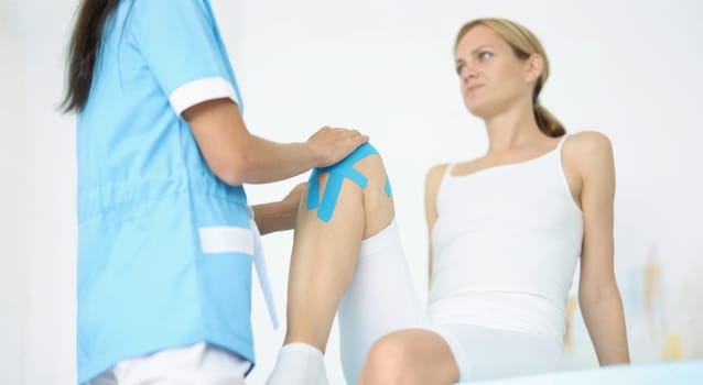 Doctor fixes kinesio tape on female leg. Stretching tendons and ligaments in sports concept