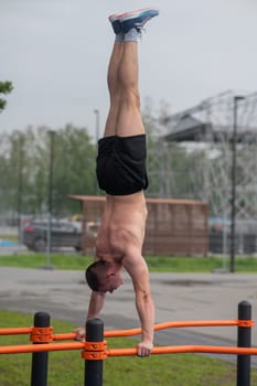 A young man doing a handstand on parallel bars outdoors. Workout