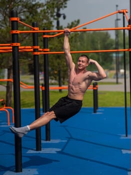 Young muscular man hanging by one hand on a horizontal bar outdoors. Vertical photo