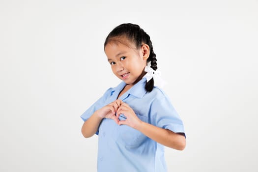 Portrait smile Asian little girl kindergarten holding hands together on chest in heart shape studio isolated white background, happy woman kid wear school uniform showing heart gesture, back to school