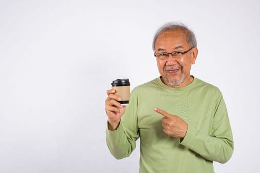 Portrait Asian old man while holding a hot coffee cup and pointing to it studio shot isolated on white background. Concept of relaxation and enjoyment, happy grandfather is enjoy his coffee takeaway