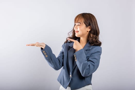 Asian Thai happy portrait beautiful young business woman standing to hold something on palm away side and point the finger side, studio shot isolated on white background with copy space