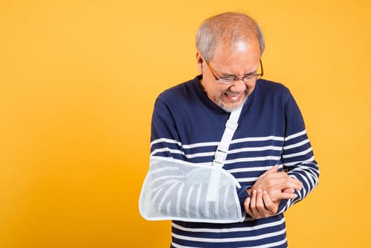 Portrait Asian old man cast on his arm painful emotions studio shot isolated yellow background, retired elderly man after accident broken arm wear arm splint for treatment accident insurance concept