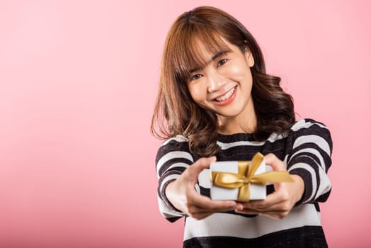 Portrait of happy beautiful Asian young woman smiling holding small gift box on hands, studio shot isolated on pink background, gift for you. Birthday, New year, Christmas, valentine day concept