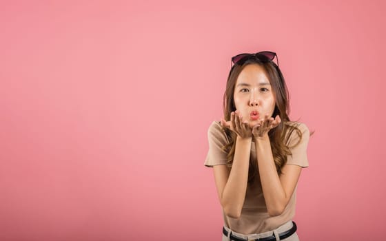 Asian happy portrait beautiful cute young woman teen standing blowing kiss air something on palm hands expresses her love looking to camera studio shot isolated on pink background with copy space