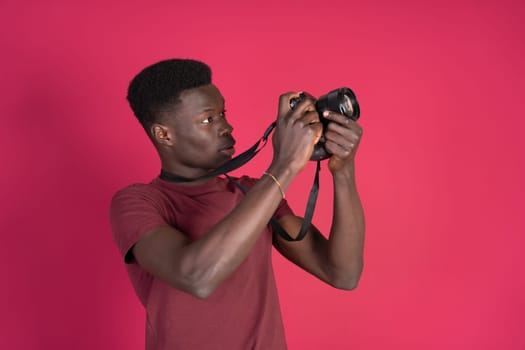A man in a red shirt is taking a picture with a camera. The man is wearing a black strap on his wrist