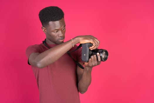 A man standing in front of a pink background holding a camera.