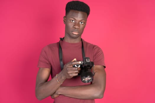 A man in a red shirt is holding a camera. He is wearing a black strap around his neck