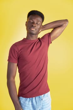 A man in a red shirt is posing for a picture. He is wearing blue jeans and has a relaxed expression on his face. The yellow background adds a pop of color to the scene