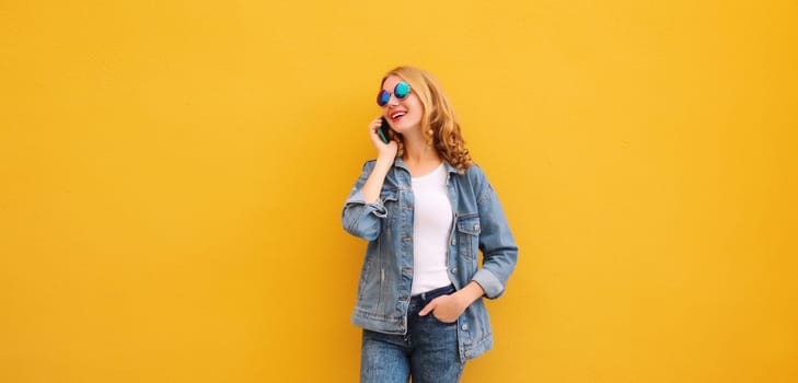 Happy cheerful young woman laughs calling on phone, girl talking on the smartphone in denim clothing looks away on bright yellow background