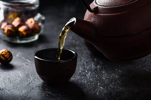 Pouring ready red tea from iron kettle into tea bowl