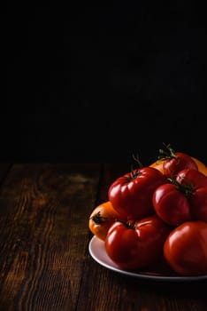 Fresh red and yellow tomatoes on white plate over wooden surface