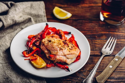 Oven baked chicken thighs with red bell peppers and lemon on white plate.