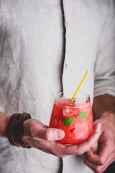 Glass of watermelon and gin cocktail with yellow straw in hands
