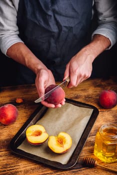 Preparing of fresh and ripe peaches with honey on baking dish. Chef halves fruits with knife.