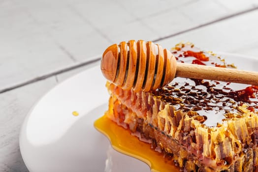 Delicious honeycomb on white plate with wooden honey dipper