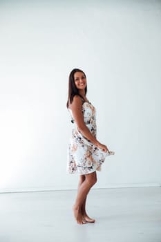woman in a floral dress poses on a white wall in a room